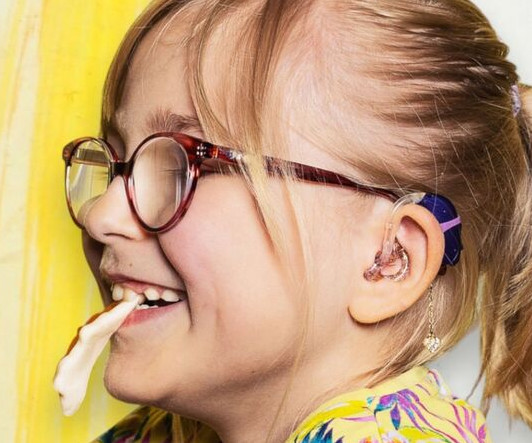 Girl eating a sweet wears diamanté heart earring in silver with hearing air